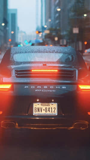黑色保時捷911 Carrera，紅色尾燈，在雨城市街黃昏行駛。 — iPhone 11 Pro 壁紙