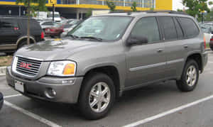 灰色GMC Envoy SUV停放在停車場，旁邊有其他汽車和一棟黃色建築物。 — 低飽和 壁紙