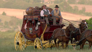 一輛紅色的 Wells Fargo 驛馬車，有兩名男子和兩匹馬在草地上移動。 — 老人 壁紙