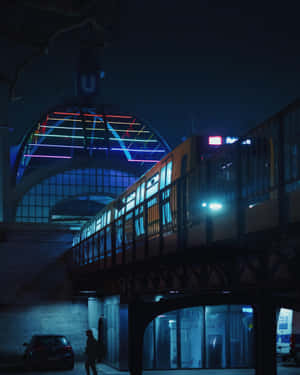 夜間，一列火車經過霓虹燈照亮的車站拱門下方，下方有一個孤獨的身影。 — 地鐵 壁紙