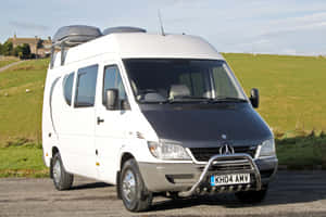 白色 Mercedes Sprinter 露營車停泊在鄉村碎石路上，背景有綠色山丘。 — Mercedes-Benz 壁紙