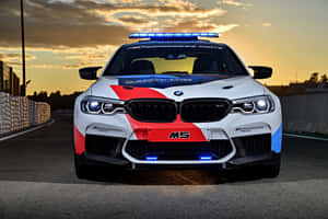 日落時分賽道上亮著閃燈的白色、紅色和藍色BMW M5賽車。 — MacBook Pro M2 壁紙