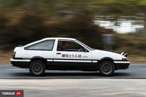 白色AE86跑車在道路上疾馳，背景模糊。 — 頭文字D 壁紙