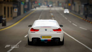 白色BMW M6跑車在黃昏時分行駛在城市街道上。
