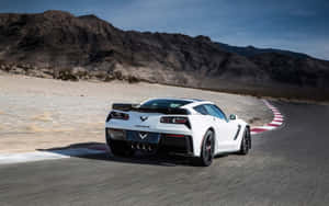 白色Corvette在沙漠賽道上奔馳，背景有山脈