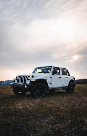 白色Jeep Wrangler停在日落時分的田野上，背景有山脈。 — Moto Pad (2026) 壁紙