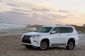 白色Lexus SUV停泊在日落時分的沙灘上，背景有海浪和碼頭。 — 凌志 壁紙