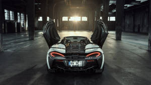 白色McLaren跑車打開車門，停在陽光普照的工業倉庫中。 — 麥拉倫 壁紙