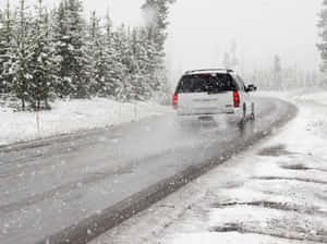 白色SUV在冬季暴風雪中行駛在積雪的森林道路上。 — 冬季風景 壁紙
