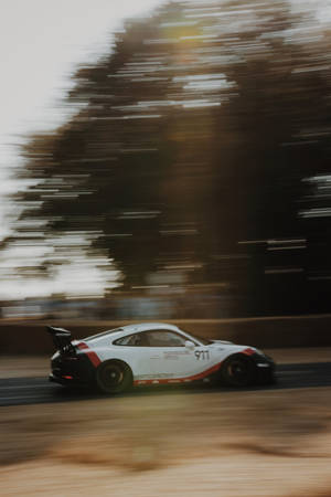白色保時捷911賽車在日落時分穿過森林，帶有動態模糊效果。 — 賽車 壁紙
