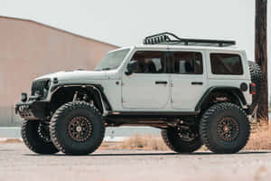 白色升高Jeep Wrangler停放在碎石上，有大輪胎和車頂行李架。 — Surface Laptop 壁紙