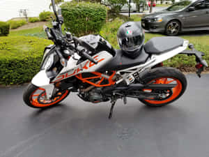 白色和橙色的KTM 390 Duke摩托車停在濕路面上，座位上有安全帽。 — 巴布風機車 壁紙