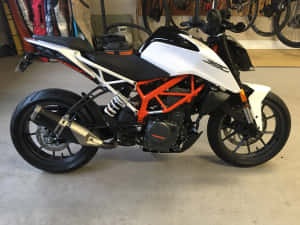 白色和橙色的KTM 390摩托車停放在車庫中，牆上掛著自行車。 — 巴布風機車 壁紙