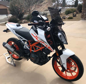 白色和橙色的KTM Duke 390摩托車停放在車道上，後面有白雪覆蓋的山脈。 — 機車 壁紙