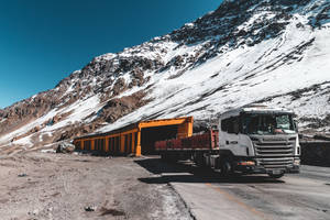 白色卡車在雪山路上經過橙色隧道，藍天白雲。 — 卡車 壁紙