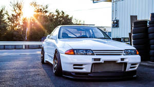 白色日產Skyline GT-R在日落時停在堆疊輪胎附近。 — 日落 壁紙