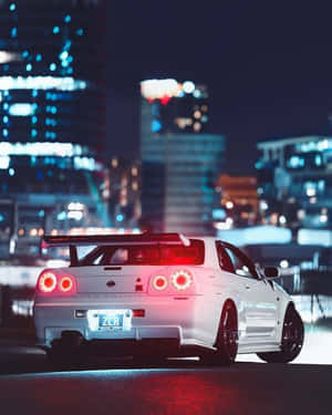 夜晚潮濕城市街道上的白色日產Skyline R34跑車，帶有發光的紅色尾燈。 — 日產 壁紙