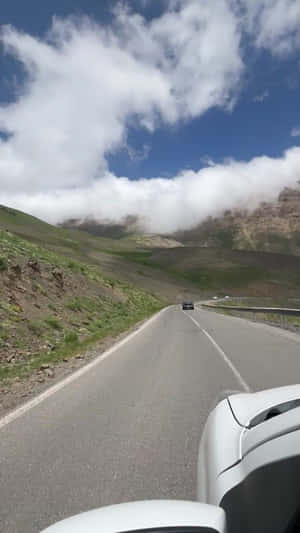 白色汽車在蜿蜒的山路上，有雲和藍天 — 手機 壁紙