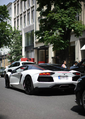 白色藍寶堅尼Aventador停在有樹木和建築物的城市街道上。 — OnePlus Pad 壁紙
