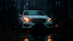白色賓士汽車亮著車頭燈在夜間行駛於下雨的黑暗森林。 — Mercedes Benz C300 壁紙