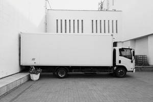 白色送貨車停在一棟現代建築旁邊，建築有垂直窗戶。 — 卡車 壁紙