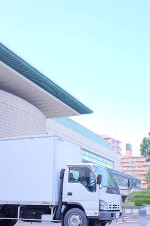 白色送貨車停泊在現代建築附近，建築有青綠色屋頂，天空晴朗蔚藍。 — 卡車 壁紙