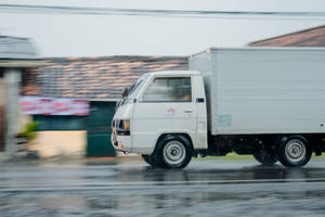 白色送貨車在雨天城市街道上快速移動，周圍環境模糊。 — 卡車 壁紙