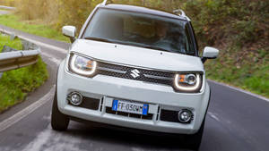 白色鈴木 Jimny 在蜿蜒的山路上行駛，周圍綠意盎然。 — 鈴木 壁紙