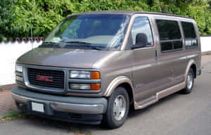 米色GMC Safari小型貨車停在車道上，背景有綠色樹木和白色圍欄。 — Steam Deck OLED 壁紙