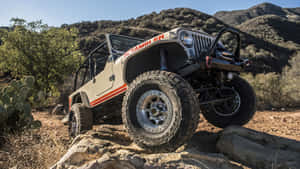 米色Jeep Scrambler在沙漠景觀中攀爬岩石，背景有山脈和仙人掌。 — 吉普 壁紙