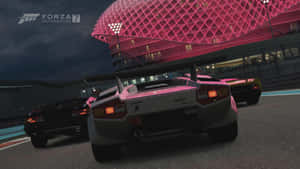 夜間在發光體育館附近的賽道上的粉紅色賽車。 — 電玩遊戲 GIF 壁紙