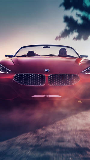 紅色BMW Z4敞篷跑車在日落時分於塵土飛揚的道路上奔馳，伴隨著棕櫚樹。 — 紅色美學 iPhone 壁紙