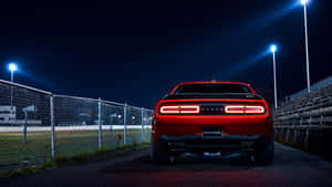 紅色Dodge Challenger在夜間停泊在體育場燈光下，靠近圍欄和看台。 — 道奇挑戰者 壁紙