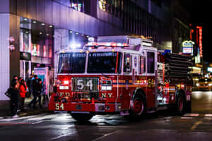 紅色FDNY消防車停在夜晚濕漉漉的城市街道上，有霓虹燈和行人。 — 消防車 壁紙