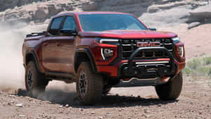 紅色GMC Canyon AT4卡車在塵土飛揚的沙漠地形上行駛。 — 低調 壁紙