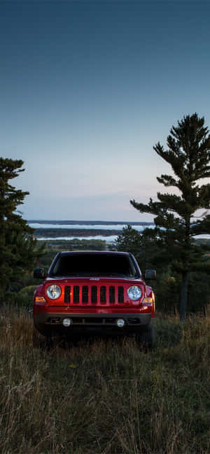 紅色Jeep Wrangler在黃昏時停放在湖邊的草地上 — iPhone 16 Pro Max 壁紙