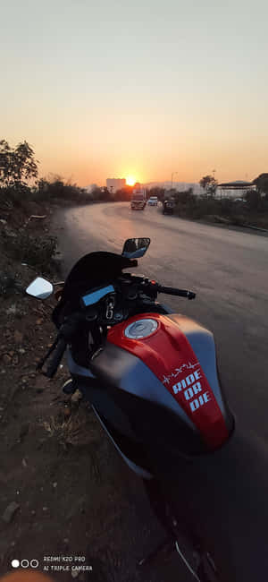 夕陽下，紅黑色機車停在路邊，遠處有建築物。 — Galaxy A 壁紙
