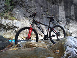 一輛登山車在岩石溪流中休息，背後懸崖上有塗鴉。
