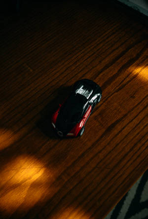 紅黑色玩具跑車在木地板上，金色陽光。 — Bugatti iPhone 壁紙