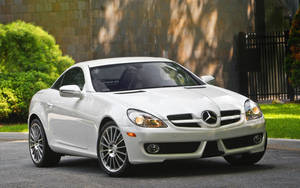 白色 Mercedes-Benz SLK 停泊在車道上，背景有綠色灌木叢和石牆。 — Mercedes Benz C300 壁紙