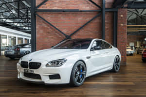 白色BMW M6轎跑車與其他車輛一起停放在磚木車庫中。 — Surface Laptop 壁紙