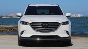 白色Mazda CX-9 SUV停泊在海邊，背景是城市天際線。 — KTM 摩托車 壁紙