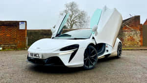 白色McLaren跑車，鷗翼車門敞開，停在磚牆附近的礫石地上。 — 麥拉倫 壁紙