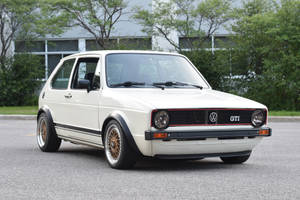 白色復古福斯Golf GTI，配金色輪圈，停在戶外樹旁。 — 福斯汽車 壁紙