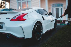 黃昏時分在屋前用水管清洗白色日產370Z Nismo的人。 — 日產 壁紙