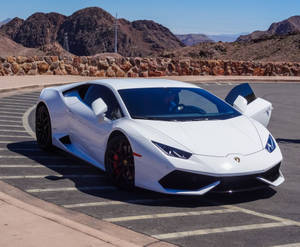 白色藍寶堅尼 Huracán 停泊在沙漠停車場，背後有山脈。 — 丘陵景觀 壁紙