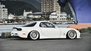 白色馬自達RX-7跑車停泊在水邊，背景是城市建築物。 — 馬自達 壁紙