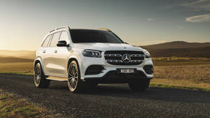 白色賓士GLS SUV停在碎石路上，背景有山丘，日落時分。 — Mercedes-Benz 壁紙