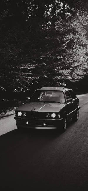 經典BMW E30房車在日落時分行駛在林間道路上。 — 汽車 iPhone 壁紙