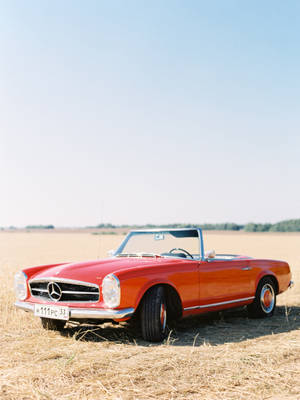 復古紅色敞篷車停放在陽光照耀的麥田中。 — Mercedes Amg iPhone 壁紙